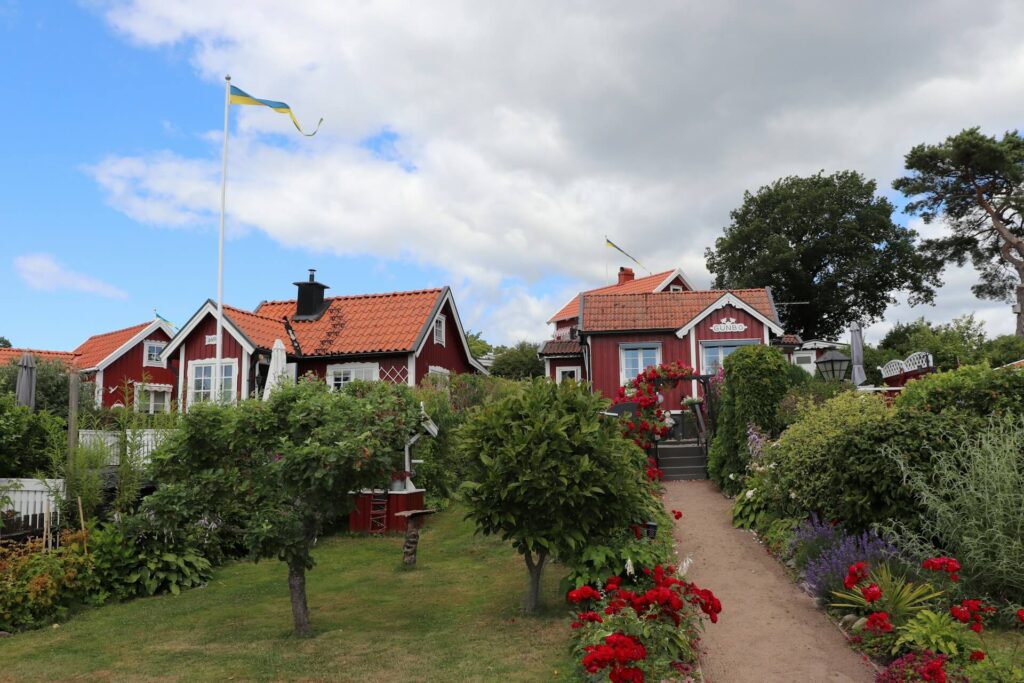 röda hus bakom en grön trädgård med röda blommor