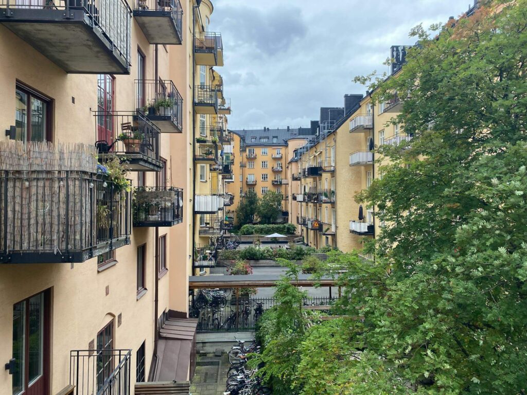 Flera lägenhetsbyggnader i gul färg med balkonger och ett stort träd vid sidan