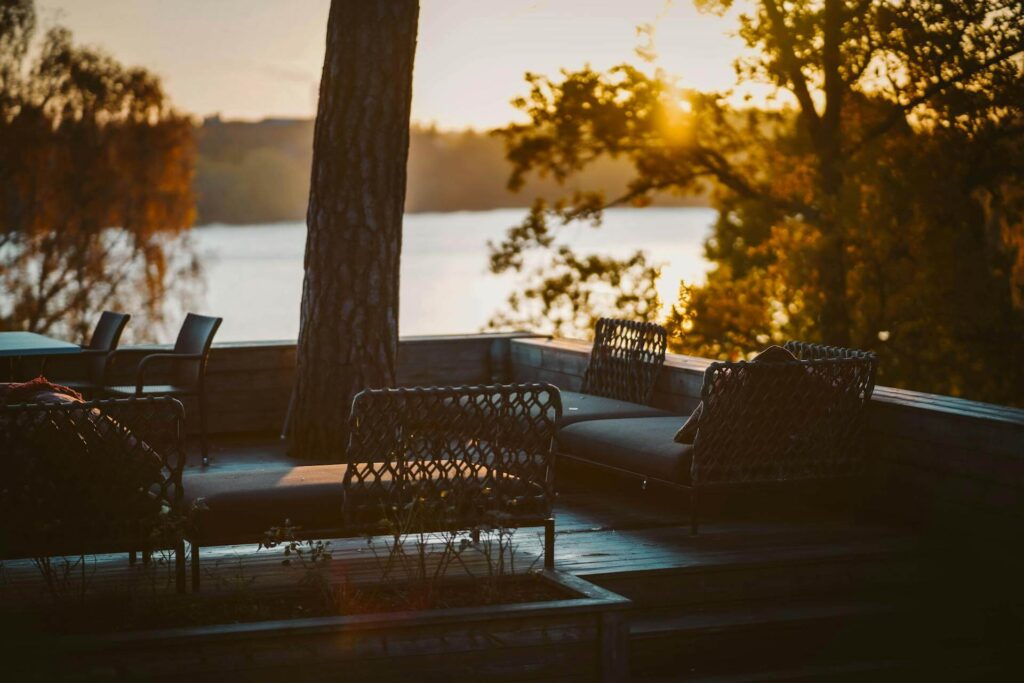 Uteplats med trägolv, ett centralt träd och soffor under en solnedgång