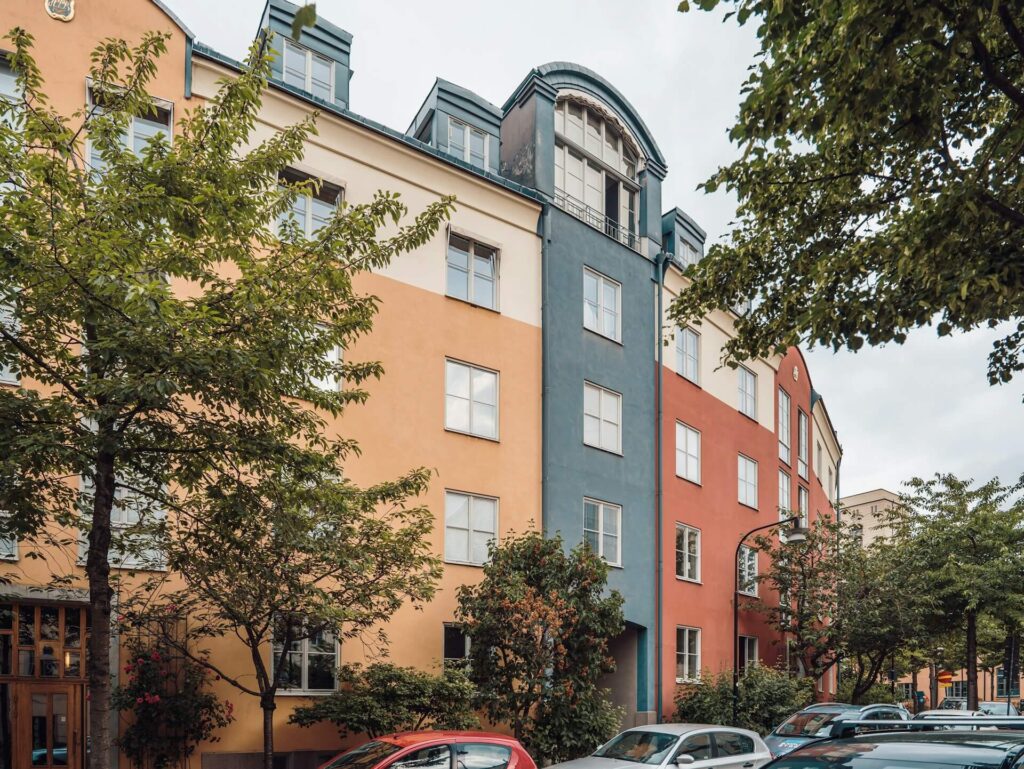 Lägenhetsbyggnad i orange, blått och vitt med träd och bilar parkerade