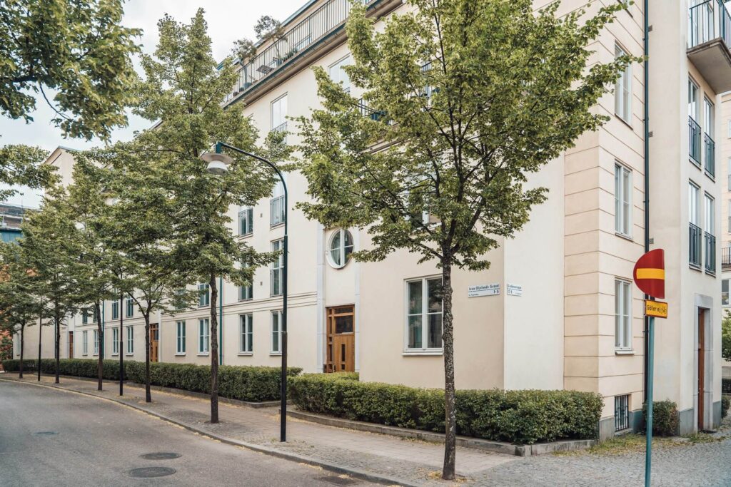 Stor vit lägenhetsbyggnad längs en gata med små och fina träd